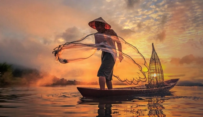 A fisherman casts a net from a boat on the Mekong Delta at sunset